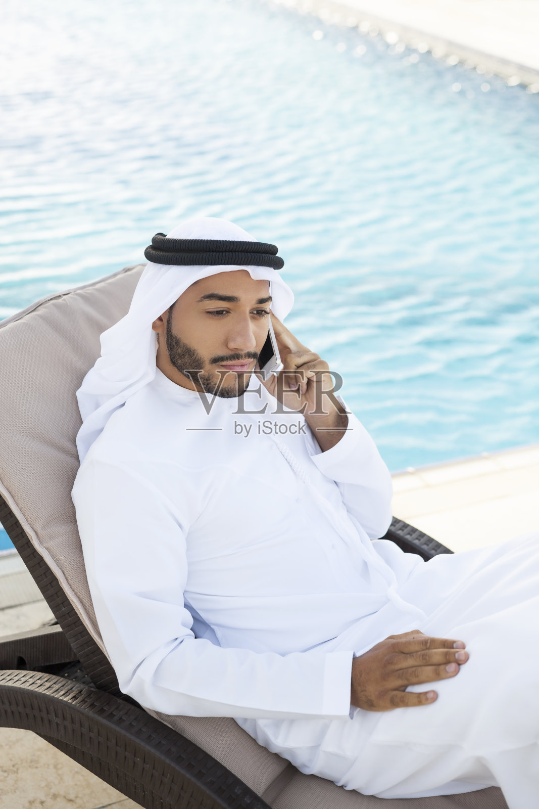 在游泳池边打电话的穆斯林男子照片摄影图片