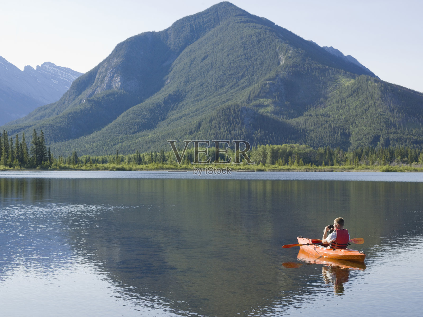年轻人划独木舟时用双筒望远镜看照片摄影图片