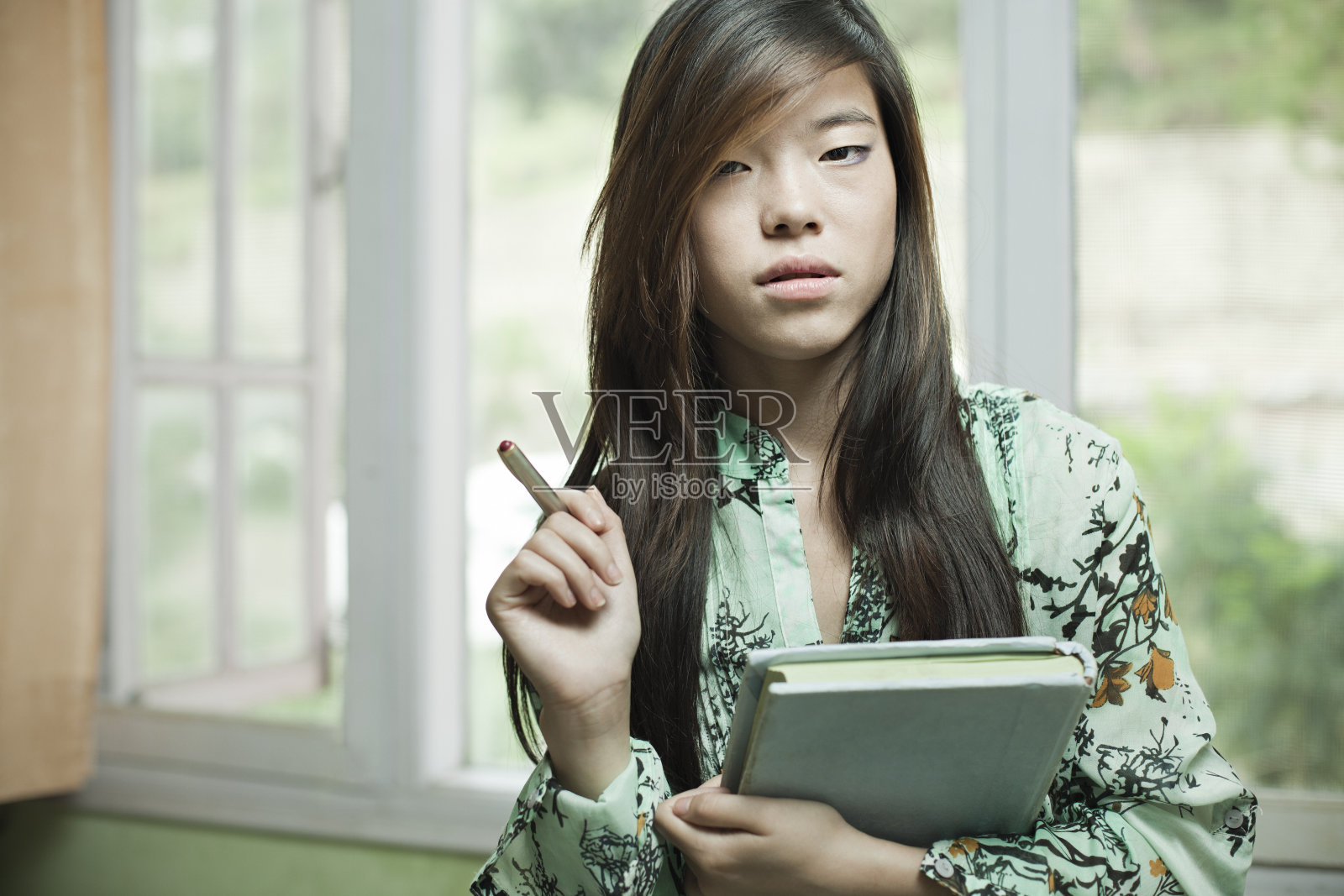 亚洲女学生拿着书和笔看着相机。照片摄影图片