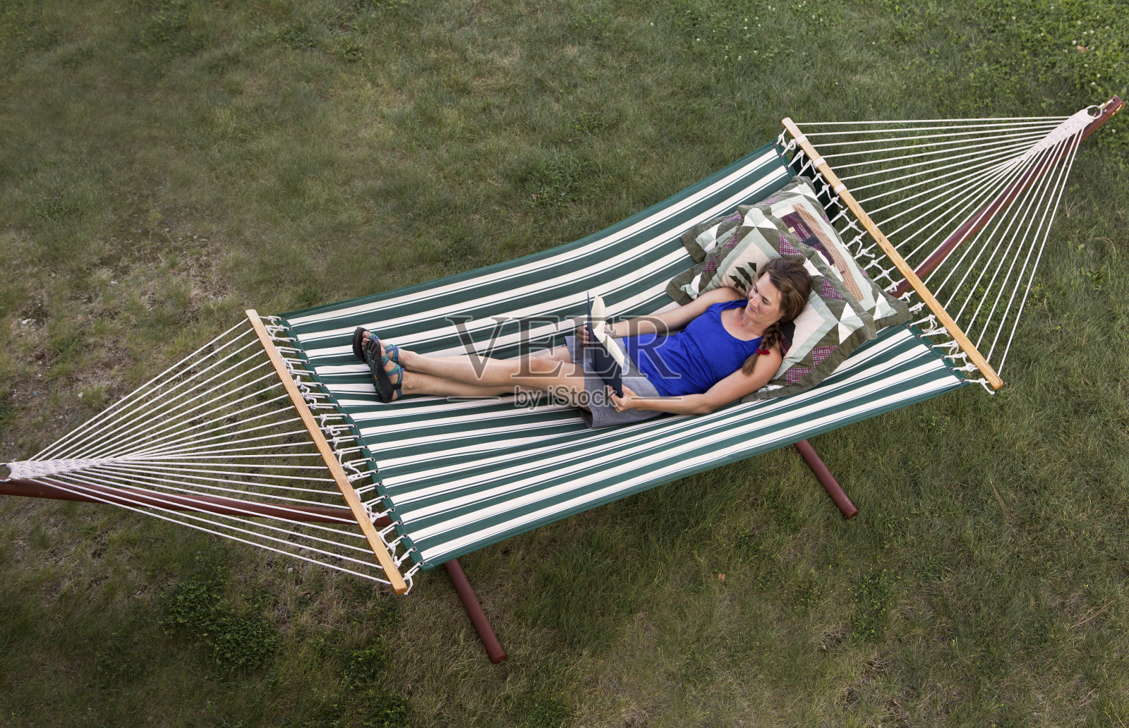 在绿白条纹吊床上看书的女人。照片摄影图片