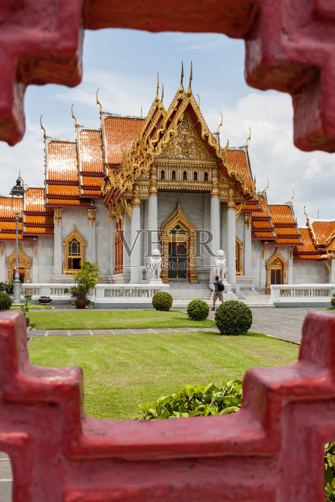 下午，游客在泰国佛寺Wat Benchamabophit的花园中拍照，透过古老的红色锻铁图案的围栏观看。照片摄影图片