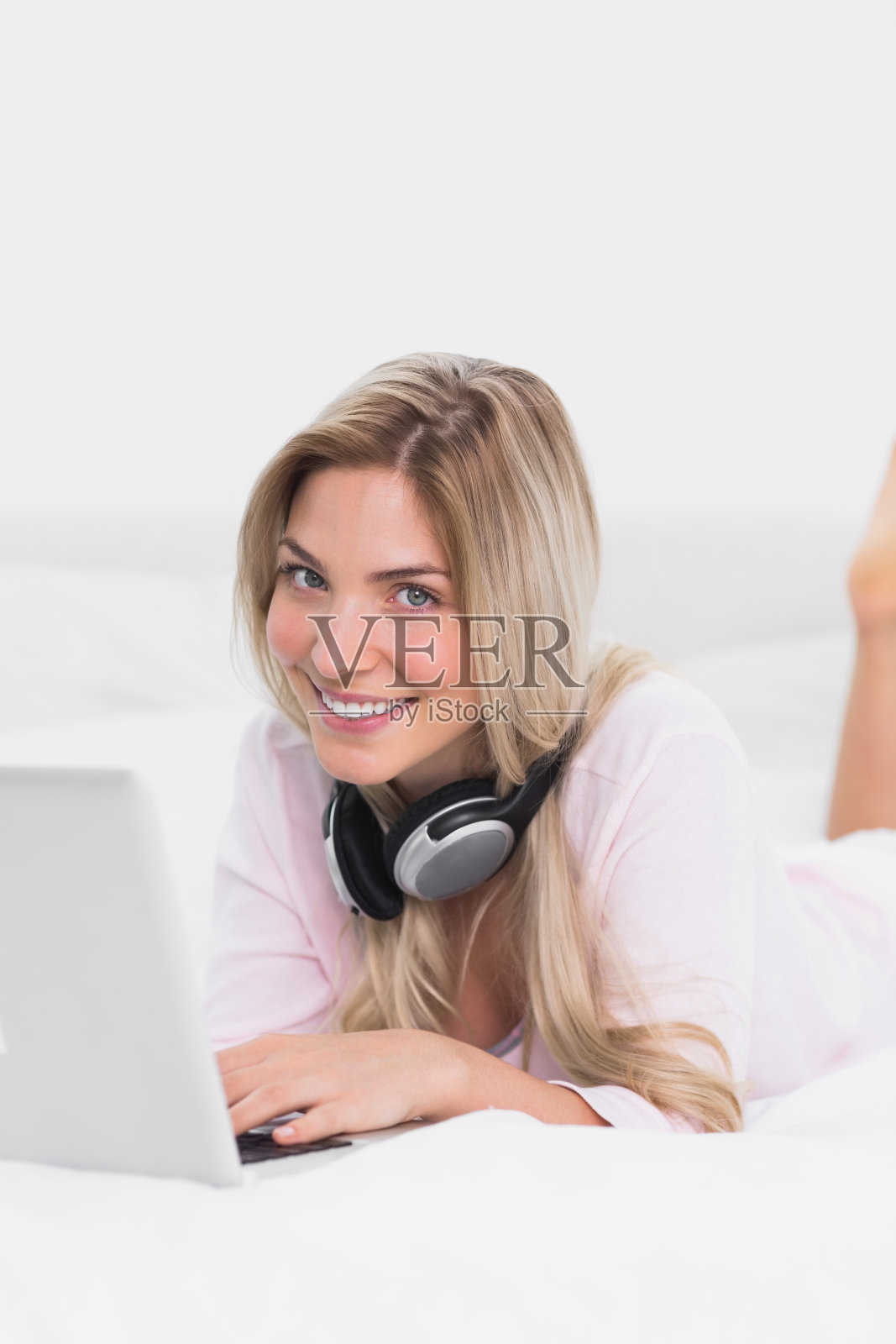 金发女人戴着耳机在床上用笔记本电脑照片摄影图片