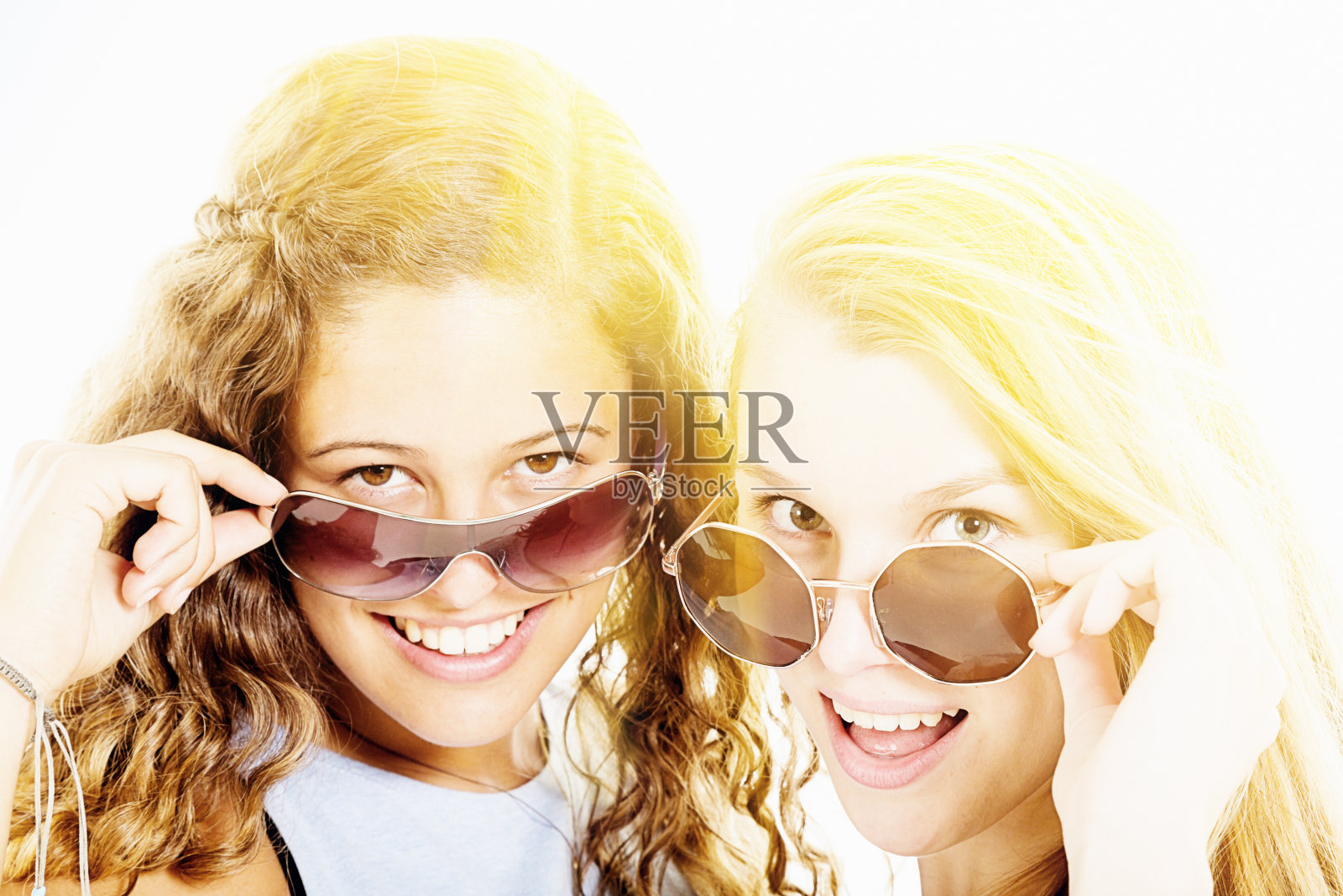 两个漂亮的女孩从太阳镜后面挑逗地窥视，微笑着照片摄影图片