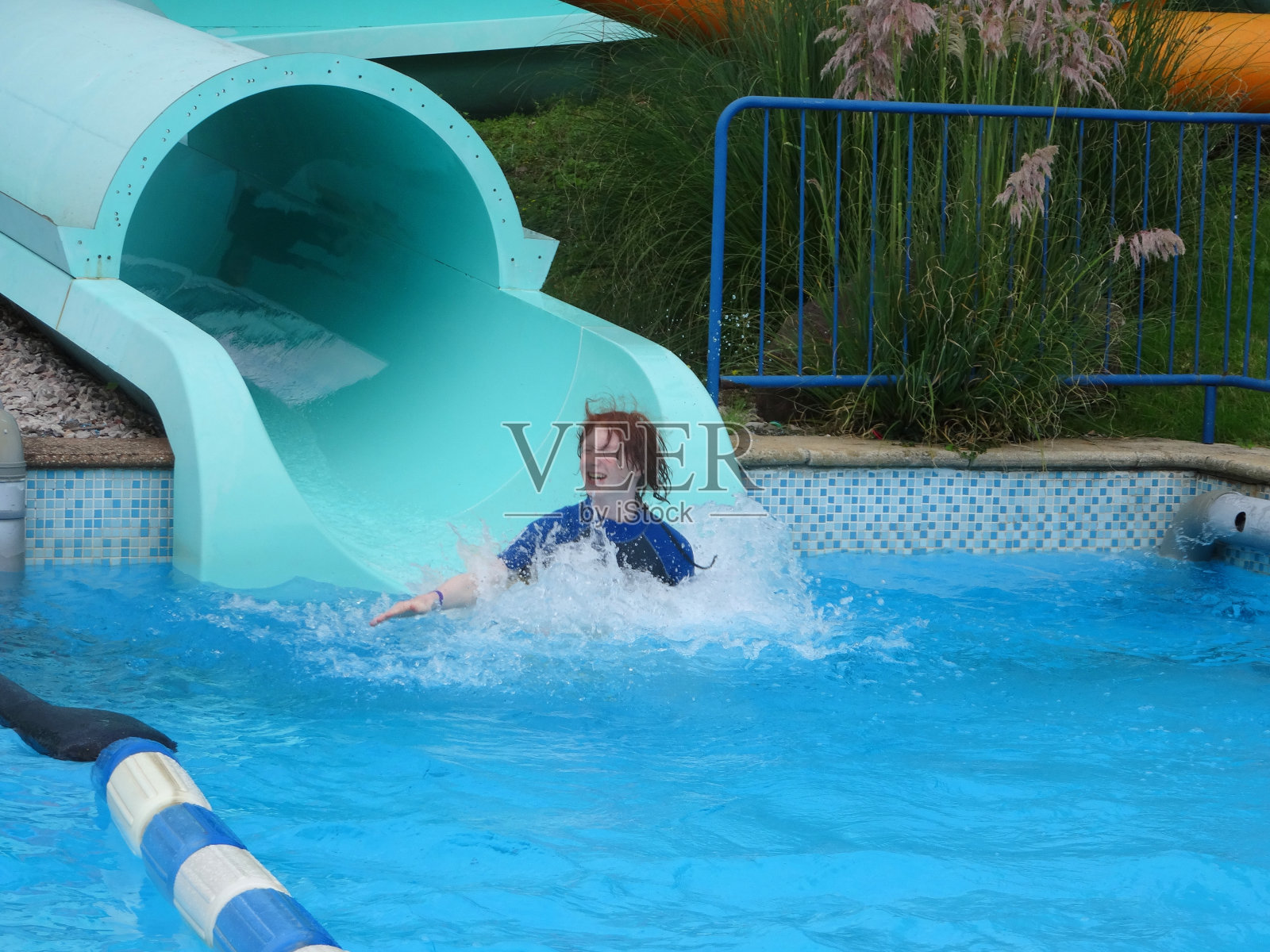 游乐园的滑水道，红发少年溅起水花照片摄影图片