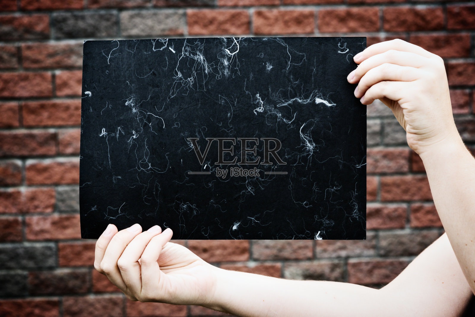 女人的手拿着一张有斑点的黑纸贴在砖头上照片摄影图片