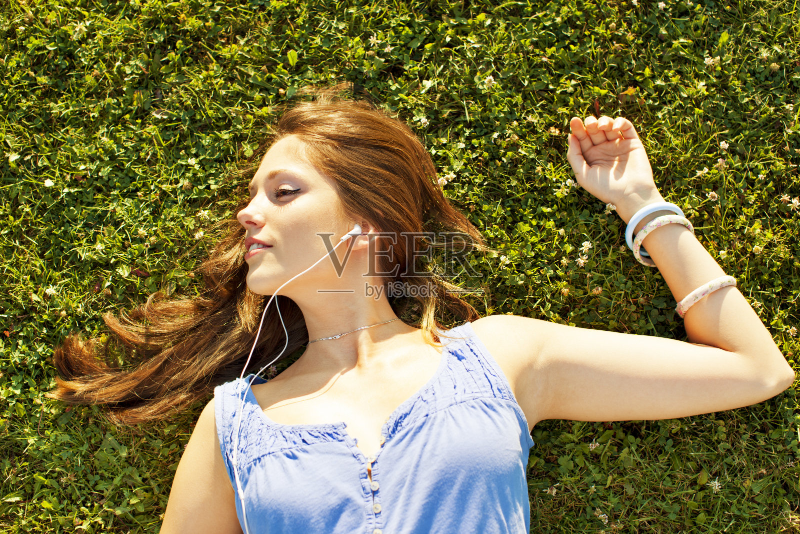 快乐的年轻女子躺在草地上听音乐。照片摄影图片
