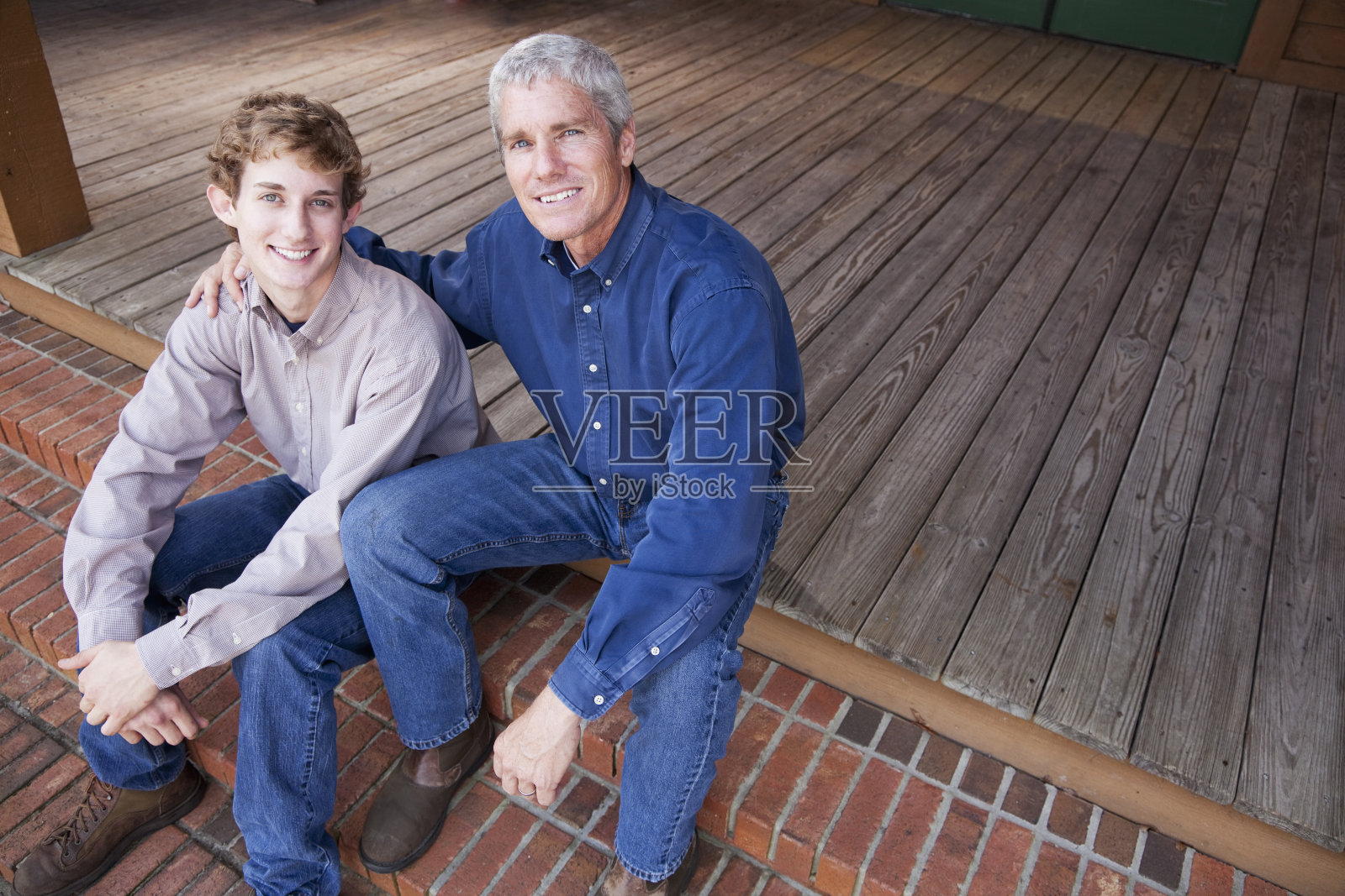 父亲和十几岁的儿子坐在门廊的台阶上照片摄影图片