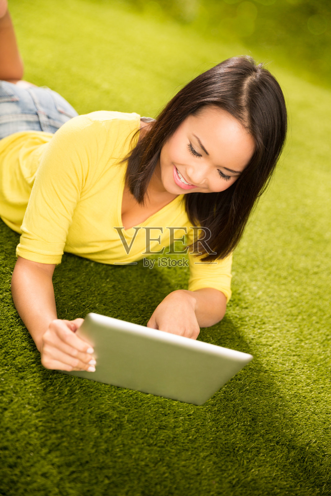 亚洲女孩躺在草地上的公园与数字平板电脑照片摄影图片