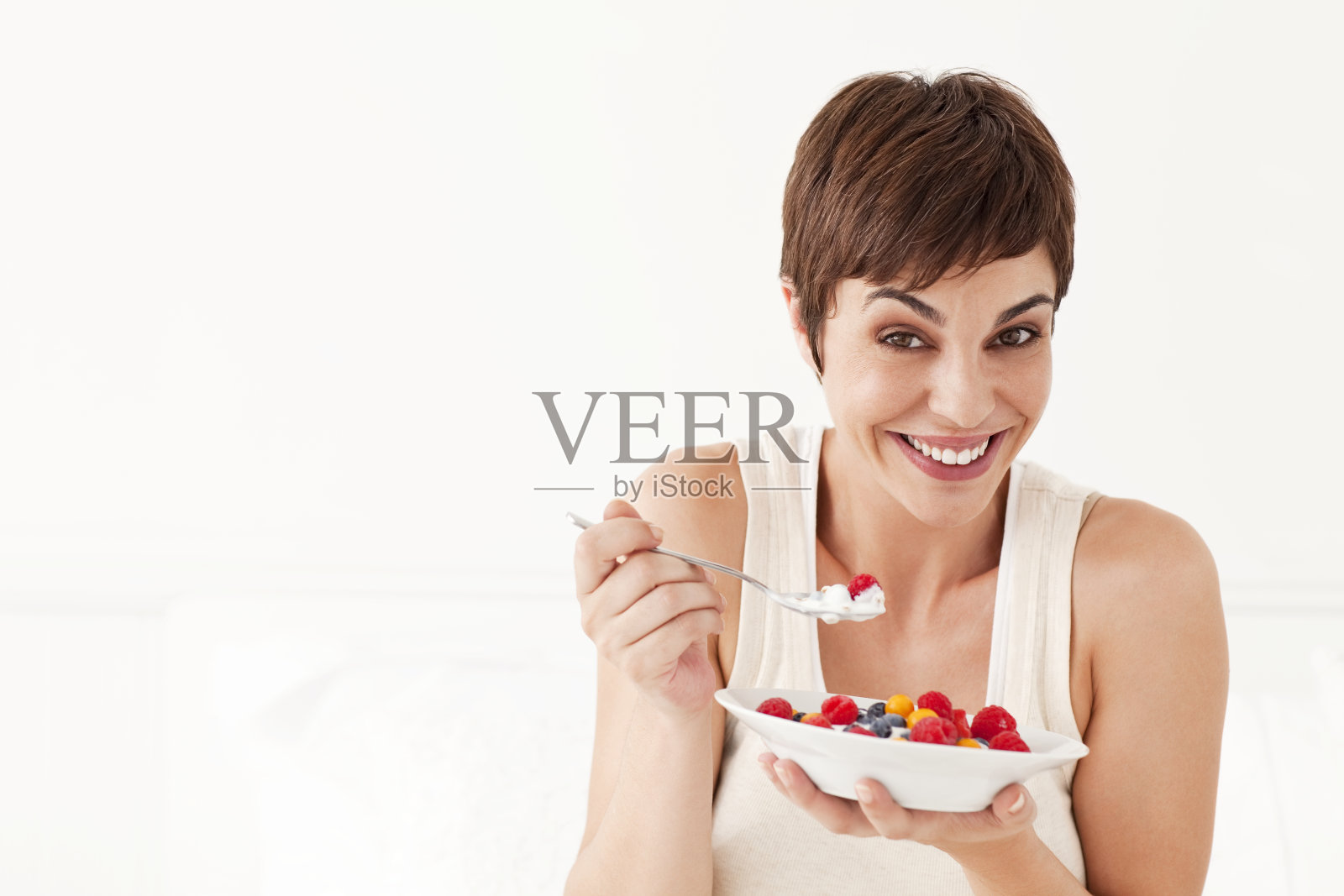 年轻女子微笑着吃着一碗水果照片摄影图片