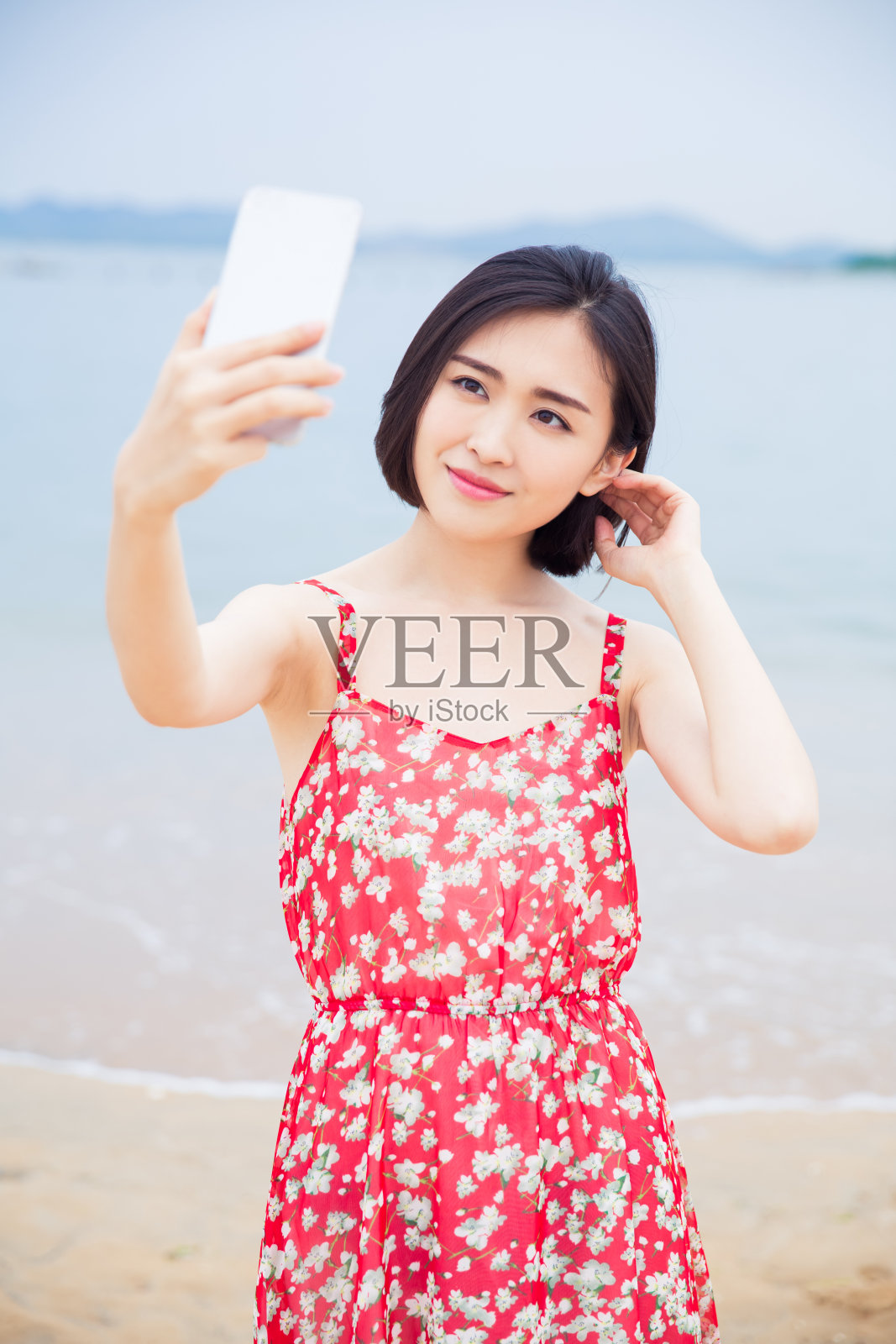 漂亮微笑的年轻女子拿着智能手机在海滩上拍照照片摄影图片