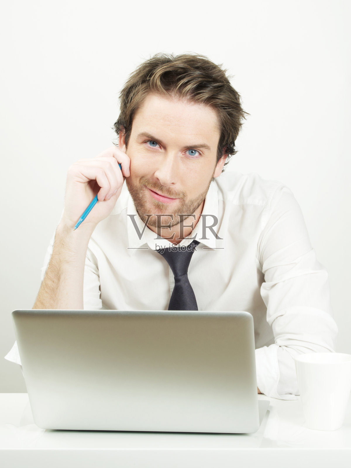 商人在手提电脑上工作，手里拿着一支笔，微笑着照片摄影图片