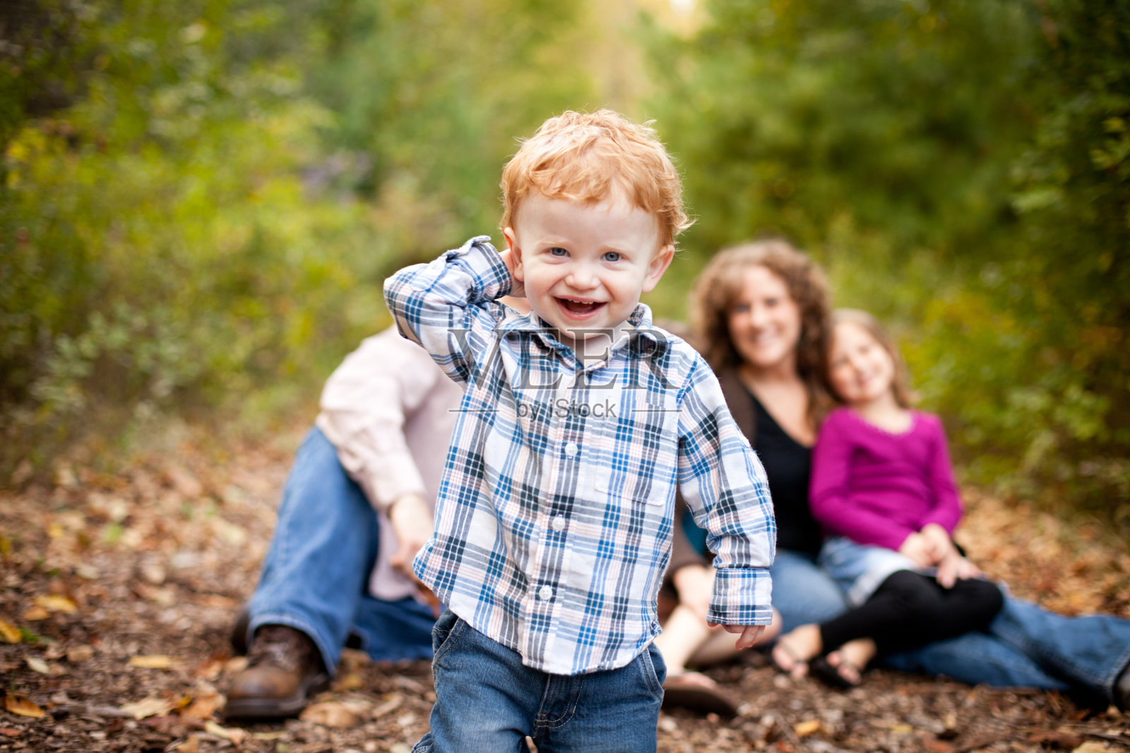 快乐的蹒跚学步的男孩和他的家庭，与秋天的树林背景照片摄影图片