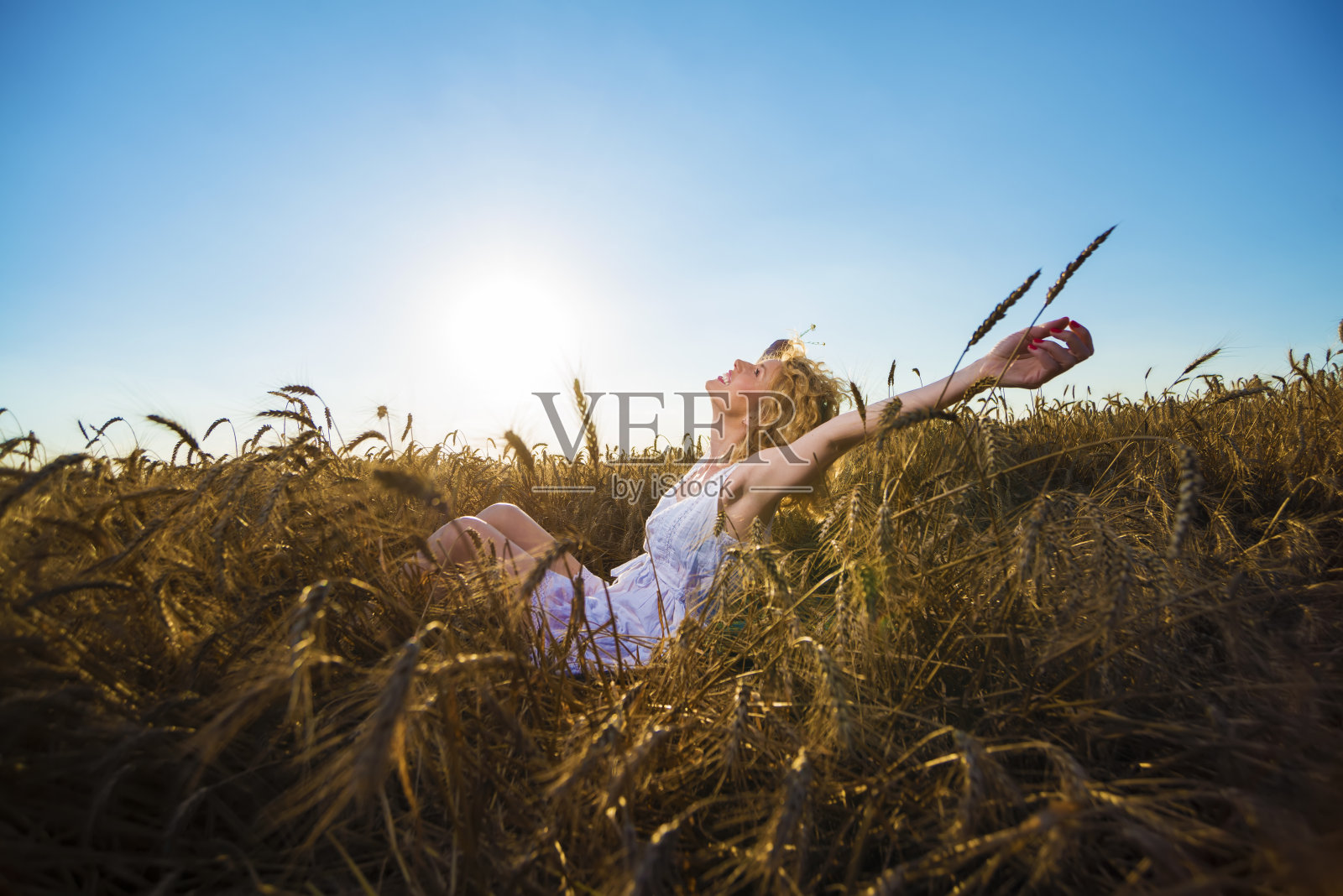 日落时分，坐在麦田里举起双手的女人照片摄影图片