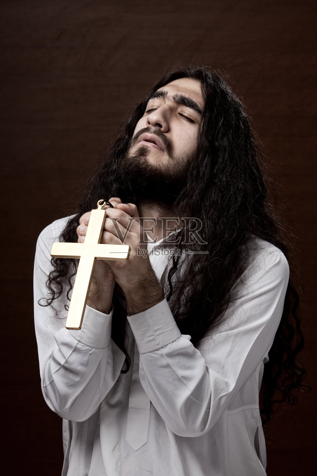 留着长发的年轻人捧着十字架祈祷照片摄影图片