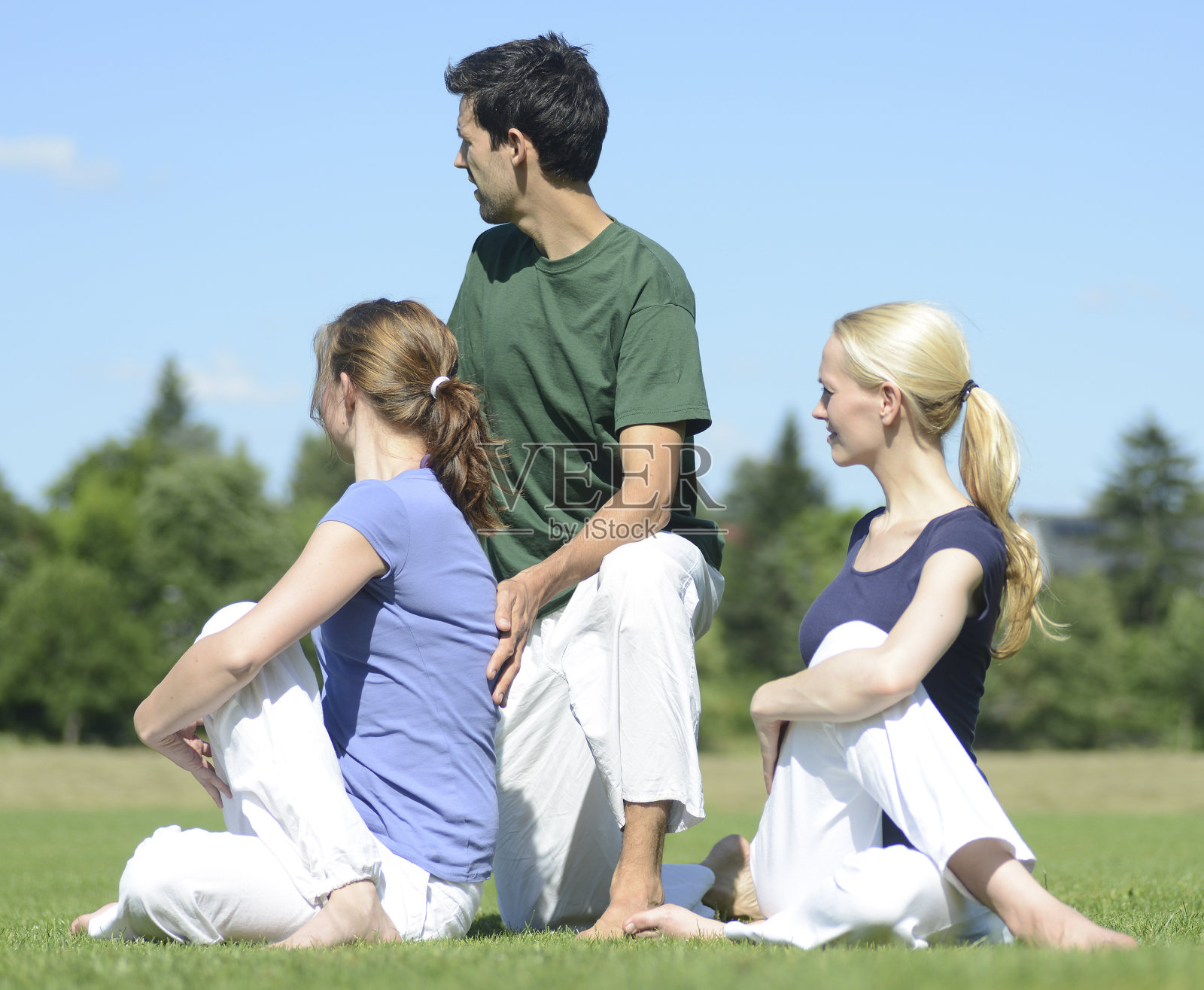 瑜伽老师在户外草地上帮助两个女孩照片摄影图片