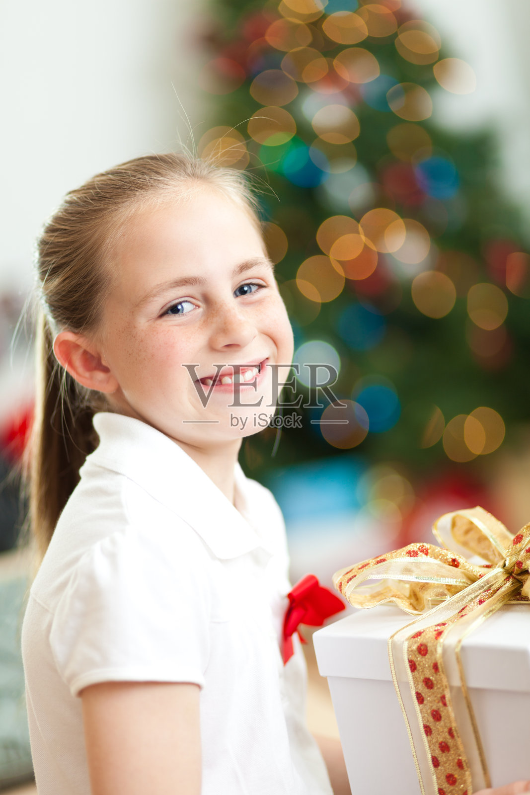 快乐的小女孩拿着她的圣诞礼物在客厅里照片摄影图片