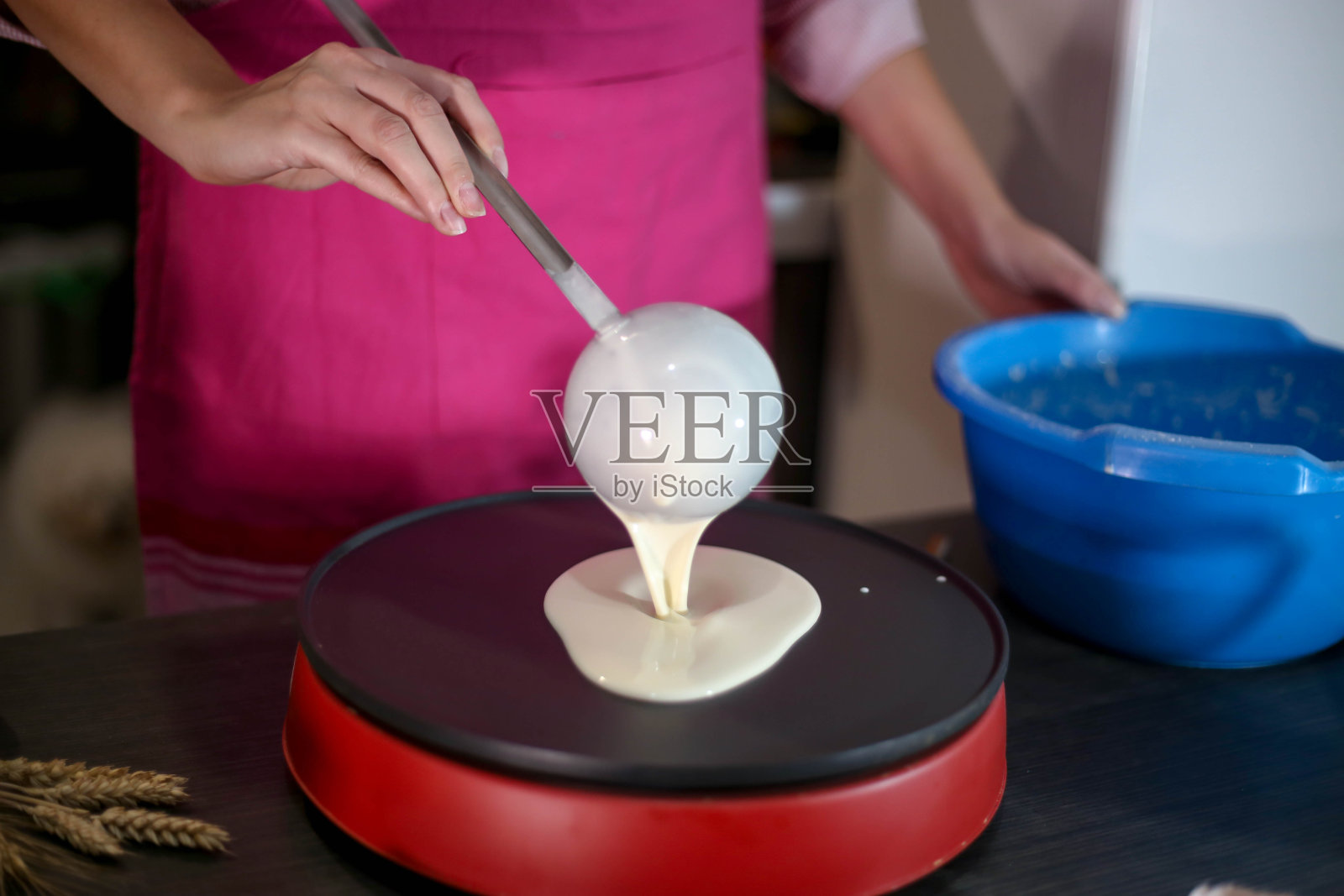 女孩倒了一勺面团做煎饼。在家做煎饼。照片摄影图片
