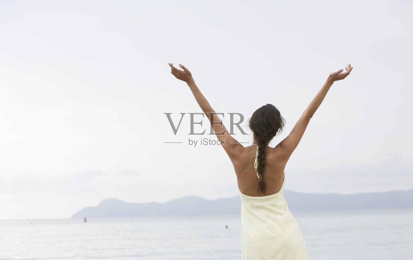 年轻女子站在沙滩上，高举双臂，后视镜照片摄影图片