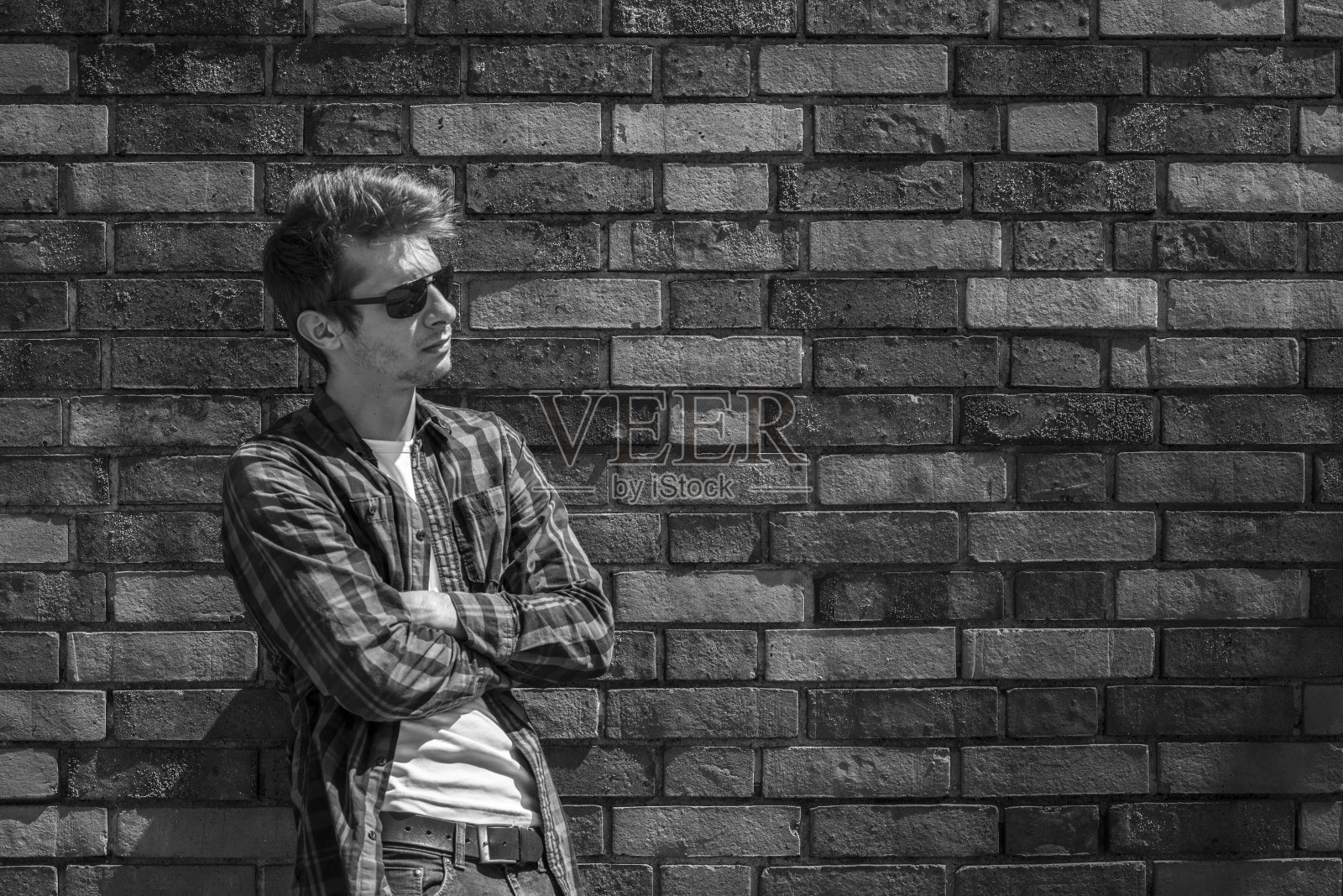 年轻人双臂交叉，靠在砖墙上照片摄影图片