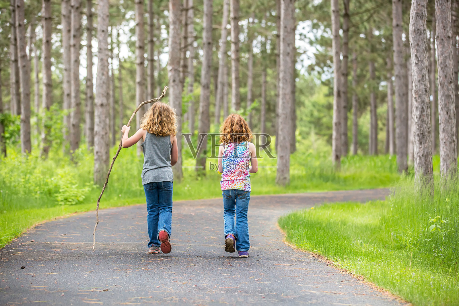 两个年轻的女孩走过铺着路面的树林照片摄影图片