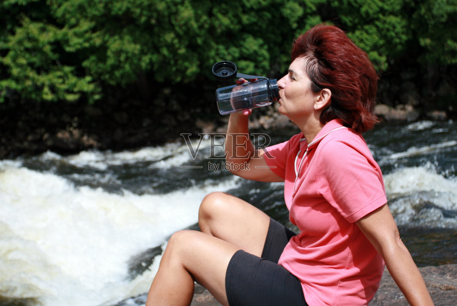 坐在河里的岩石上喝水的年长妇女照片摄影图片
