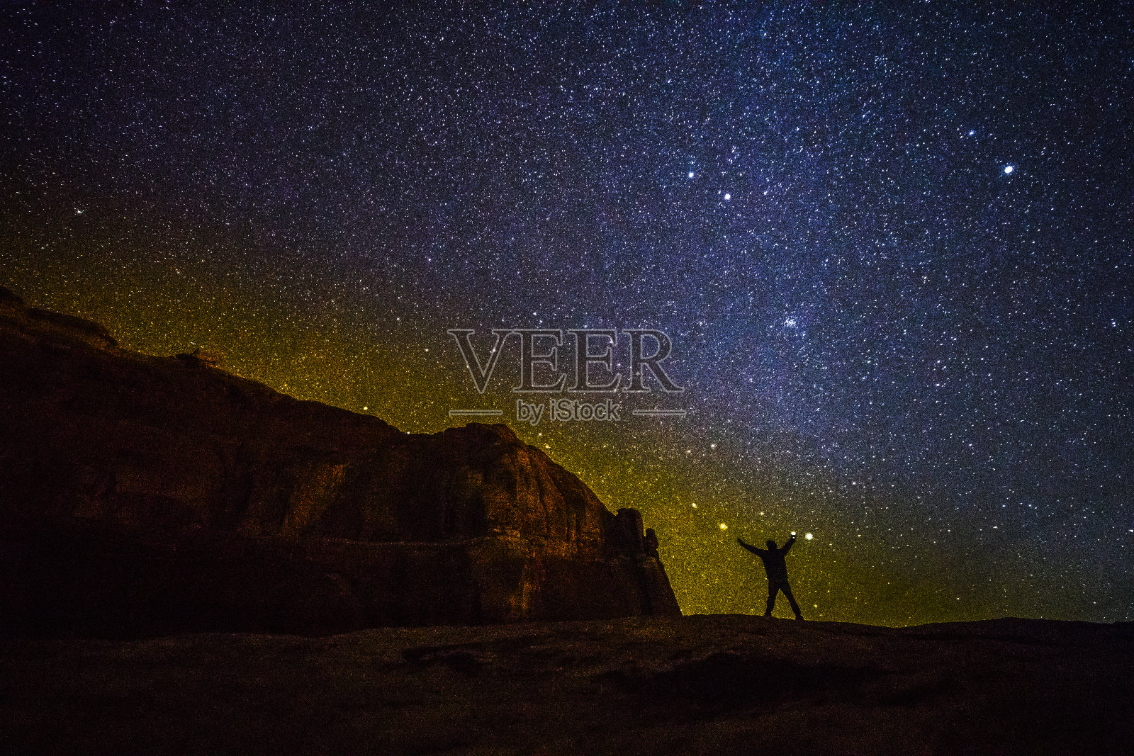 这个小个子男人站在无尽的宇宙前面。犹他州拱门国家公园山上的人的剪影，映衬着星空照片摄影图片