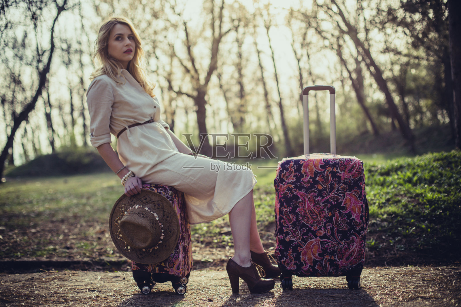 在一个夏日里，年轻的时尚女子坐在手提箱上照片摄影图片