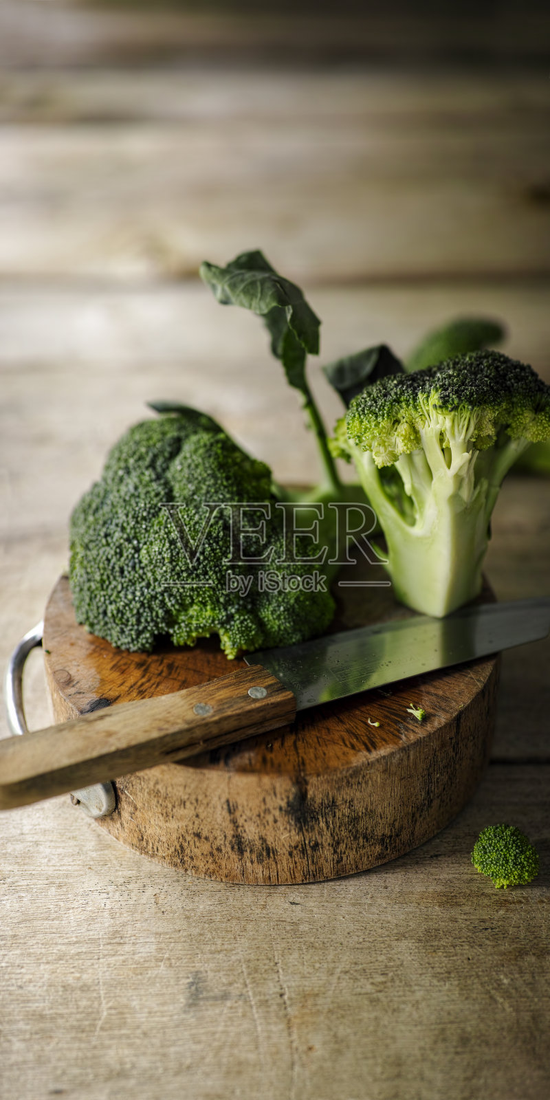把新鲜的花椰菜切成片放在一个旧的木砧板上，旁边放着一把锋利的小刀，背景放在一个旧的木头桌子上。照片摄影图片