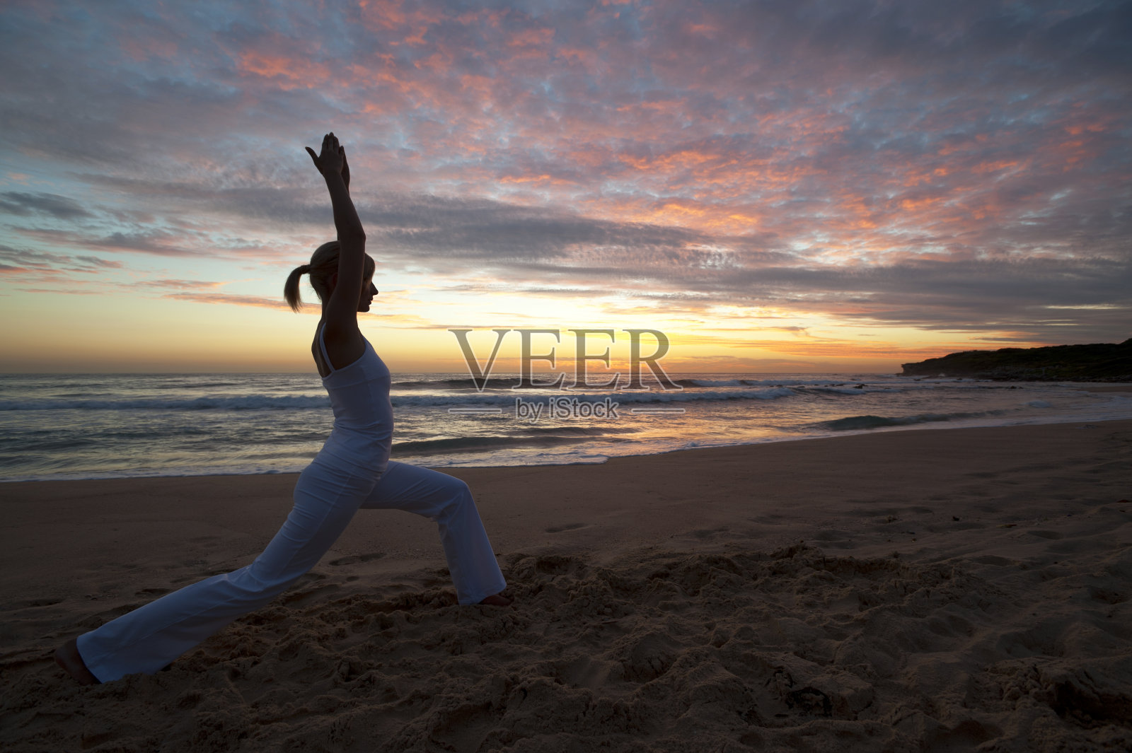 在戏剧性的天空下，在海滩上做瑜伽的女人。照片摄影图片