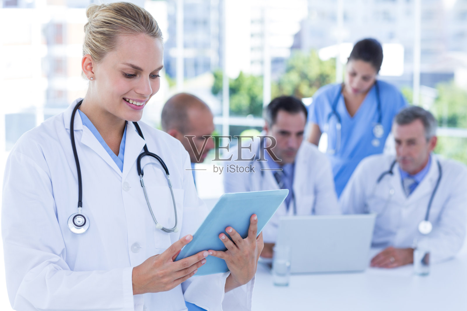 微笑的女医生看着剪贴板，而她的同事工作照片摄影图片