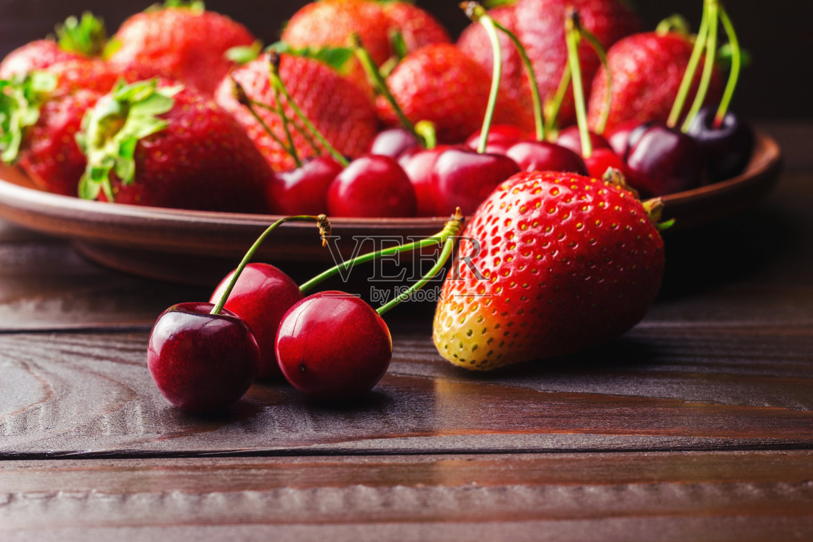 深色木板上的新鲜有机草莓和樱桃，背景是装满浆果的盘子，特写，选择性聚焦照片摄影图片
