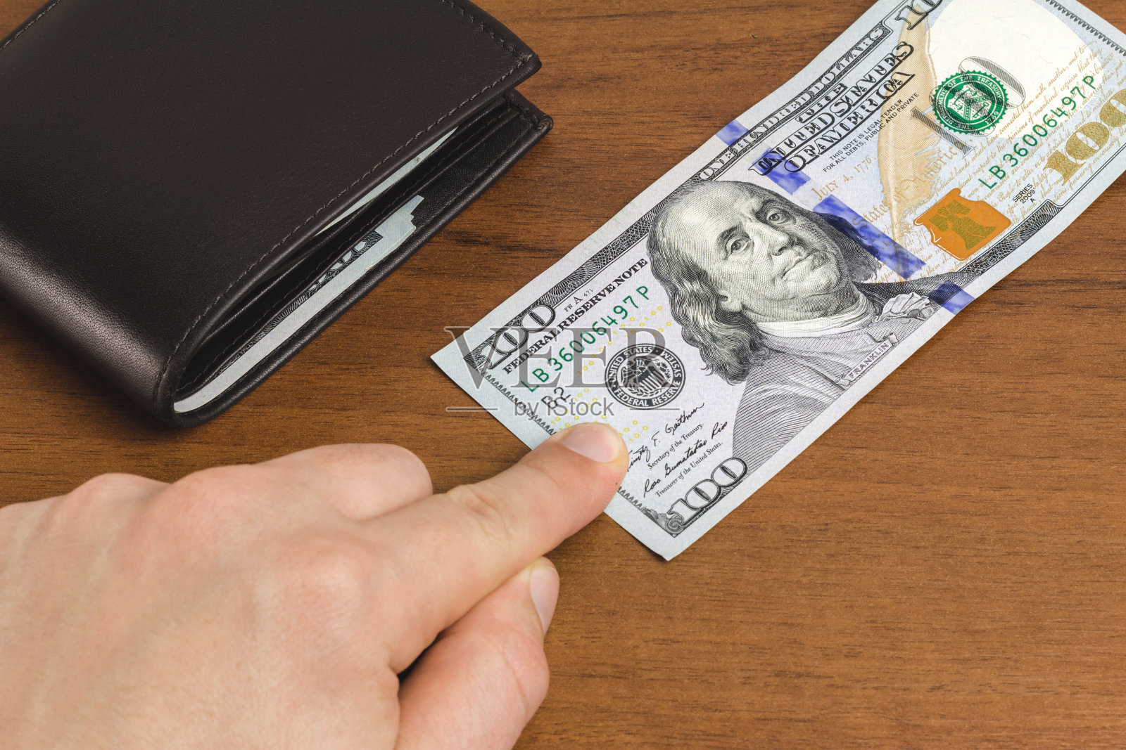 人已经把他的手指放在了百元钞票的木制背景上，特写，货币和金融的概念。照片摄影图片