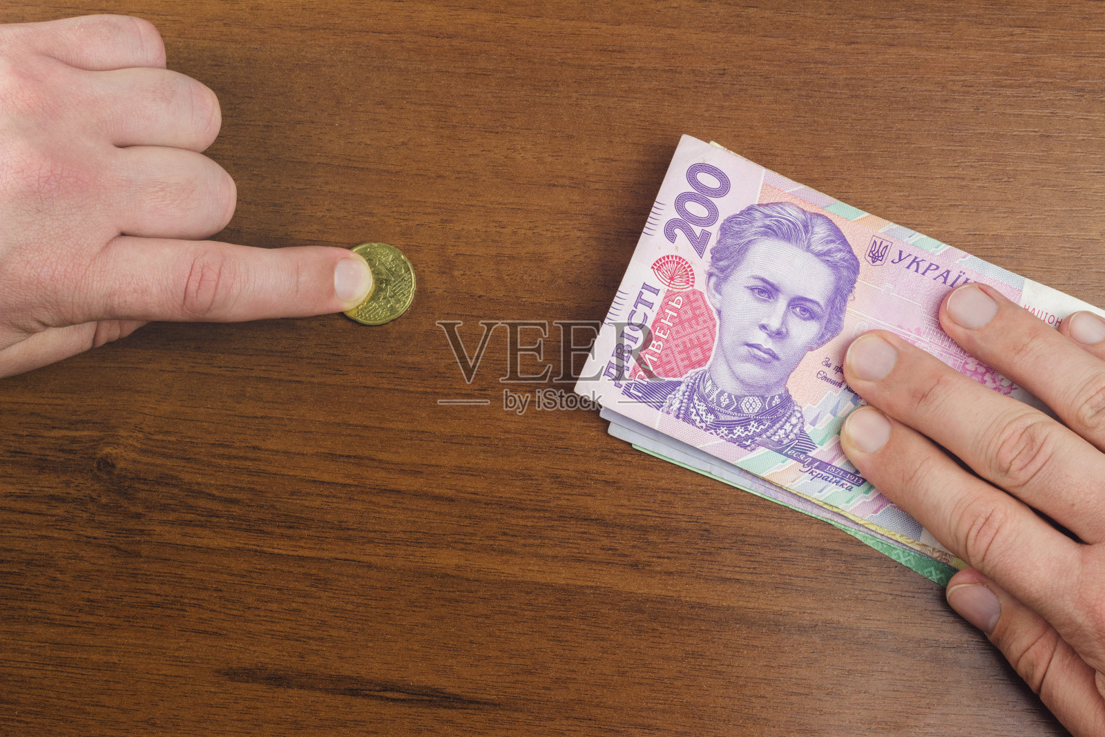 男子一手拿着一包乌克兰格里夫纳纸币，另一手拿着欧元分硬币，有贬值的概念。照片摄影图片