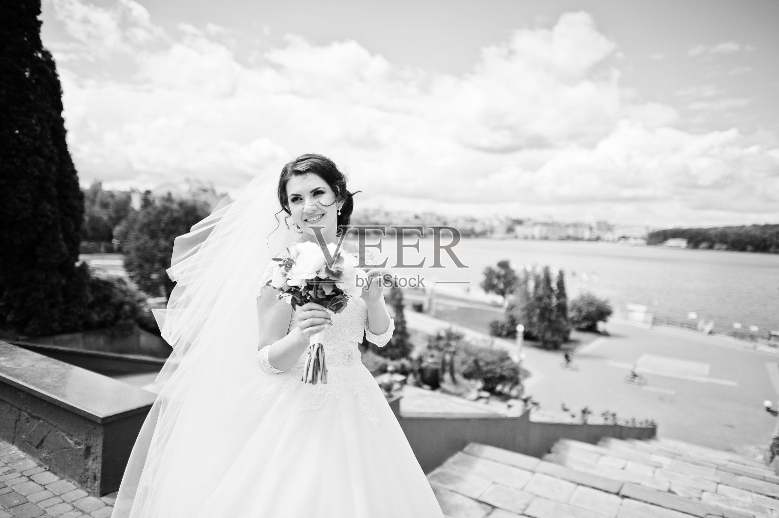 欢快的深色头发的新娘映衬着蓝天和令人惊叹的云彩背景城市湖泊。照片摄影图片