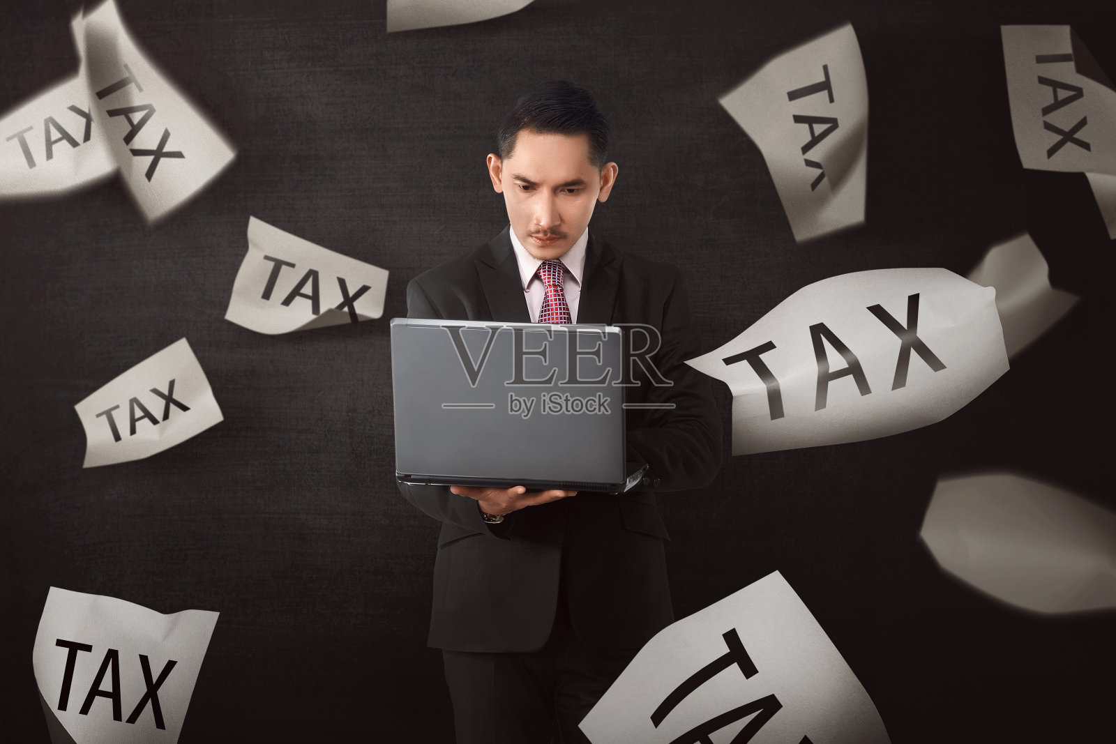 迷人的亚洲商人在笔记本电脑上工作，文字税收的下落的纸照片摄影图片