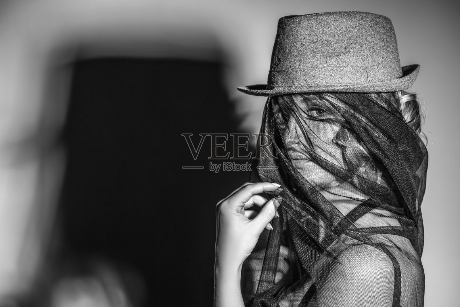 美丽的女模特戴着帽子和面纱，脸上有阴影在墙上照片摄影图片