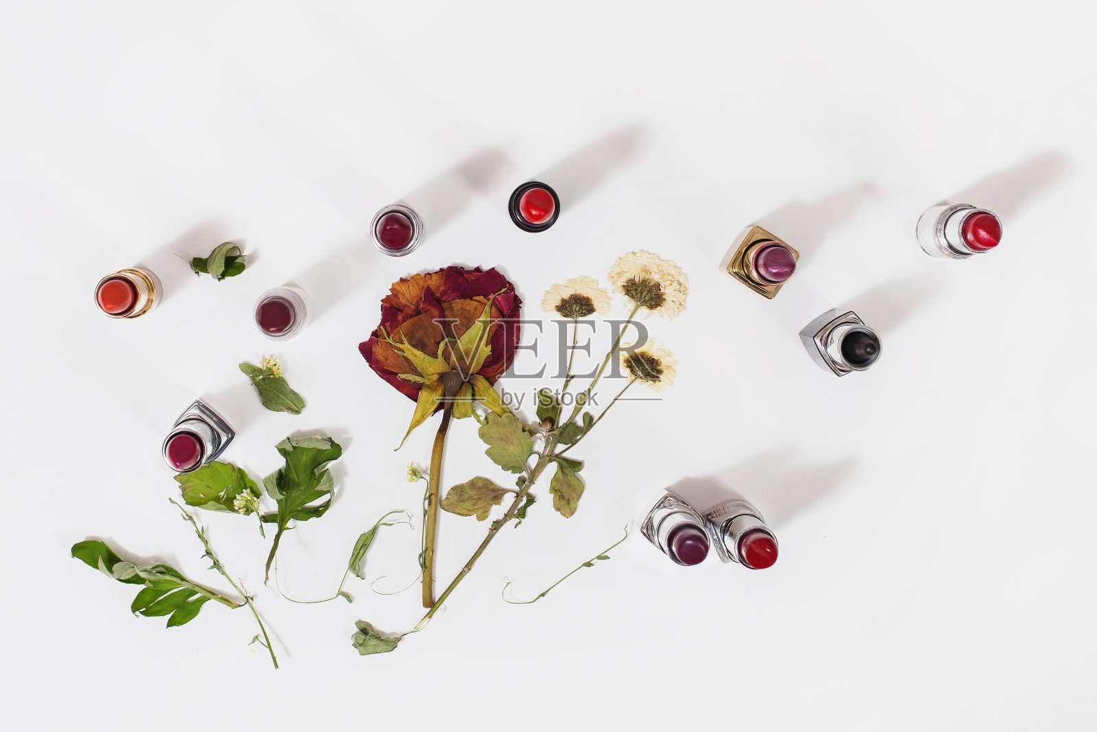 白色背景上有光泽的口红。嘴唇的装饰性化妆品。在浅面上的干花。从上面看。干玫瑰。照片摄影图片