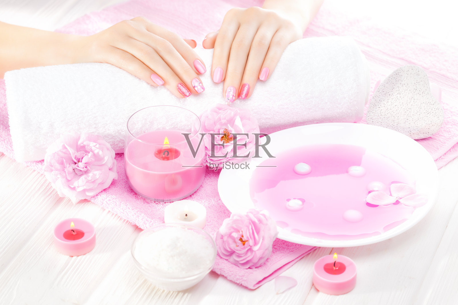 白色木桌上放着漂亮的粉红色指甲和茶玫瑰。水疗中心照片摄影图片