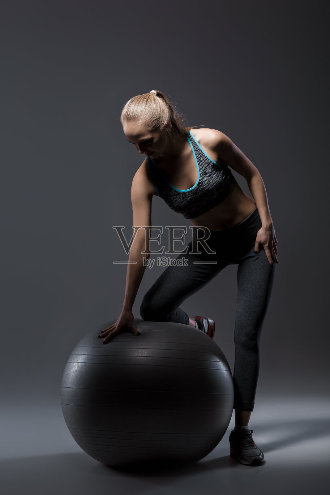 美丽的金发女孩在运动服装坐在健身球在黑暗的背景照片摄影图片