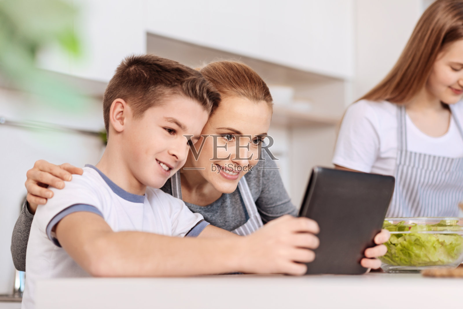 阳性母亲在厨房和儿子一起使用平板电脑照片摄影图片