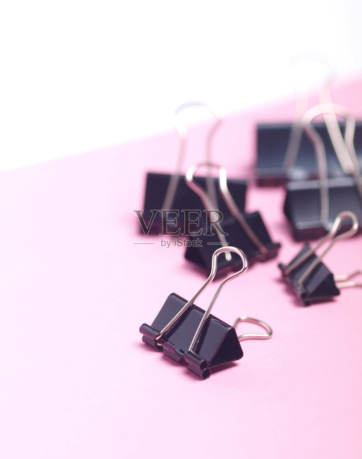 一束黑色回形针在浅粉色和白色的背景上。照片摄影图片