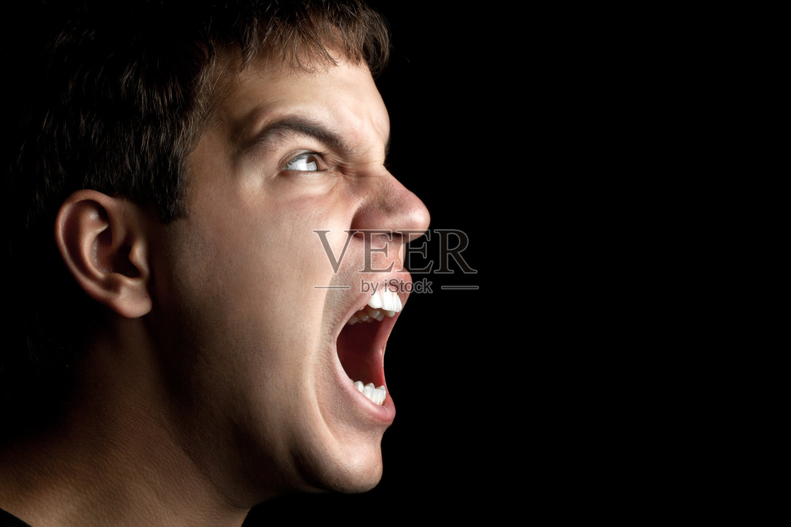 一个愤怒的年轻人在黑色背景上尖叫的肖像照片摄影图片