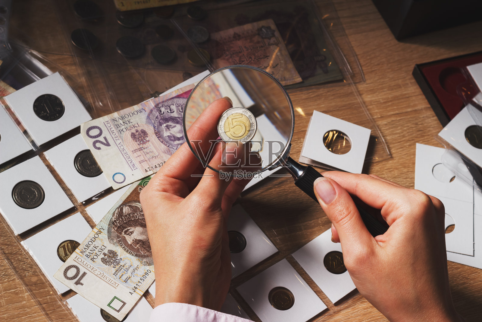 透过放大镜，那女人手里拿着一枚兹罗提金币照片摄影图片