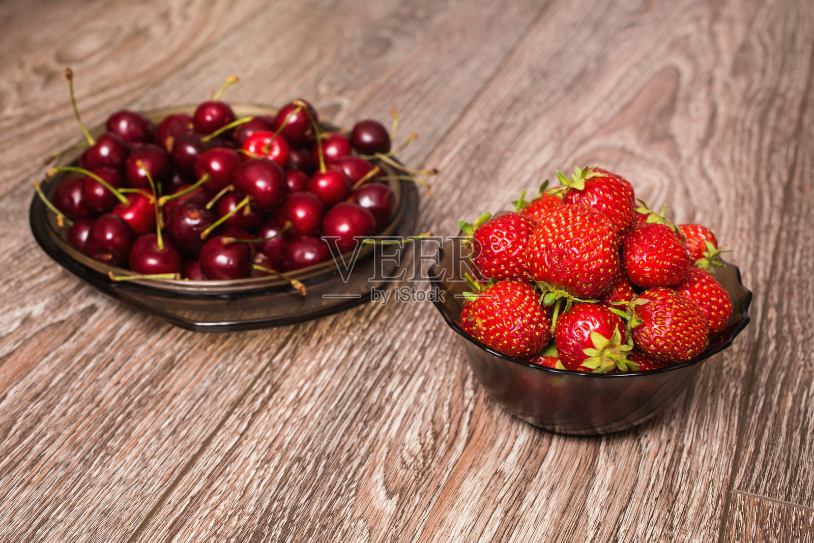 木背景上的盘子里放着一颗熟透多汁的红樱桃和一个大大的红草莓。甜蜜夏日浆果。照片摄影图片