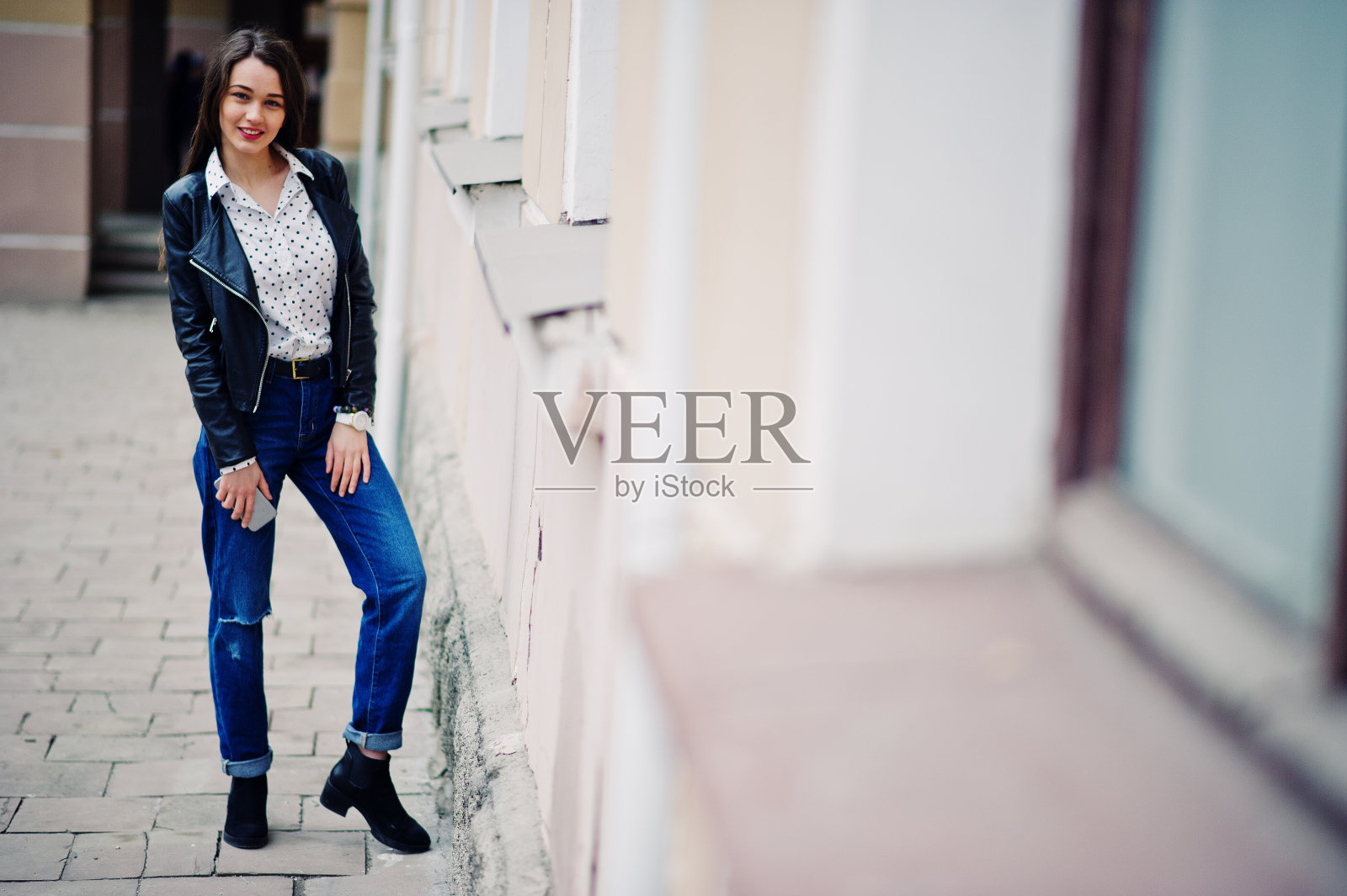 肖像时尚的年轻女孩穿着皮夹克和破洞牛仔裤与一杯咖啡。街头时尚模特的风格。照片摄影图片