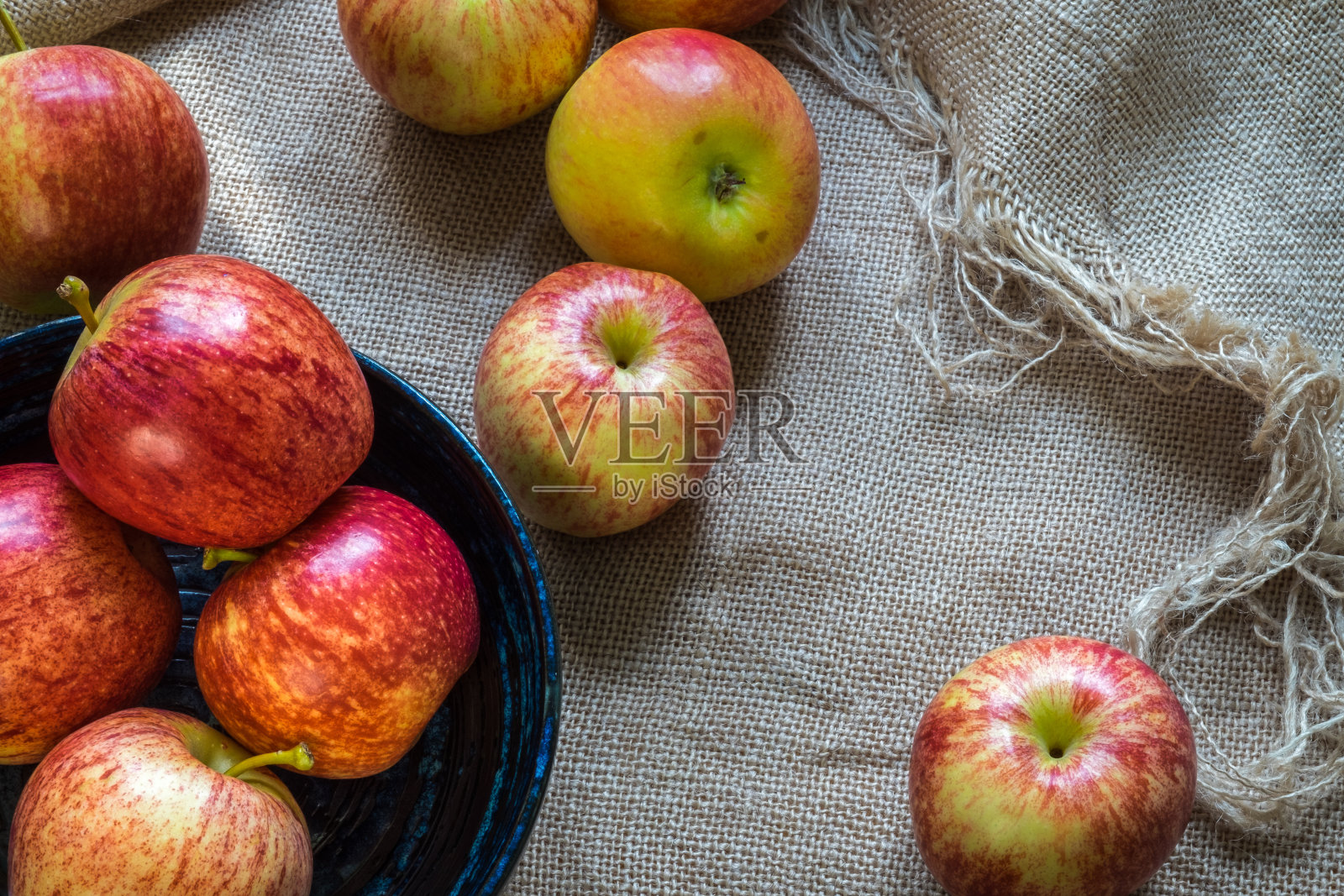 灰色粗麻布上的蓝色陶瓷板上的鲜红苹果。自然光线。照片摄影图片