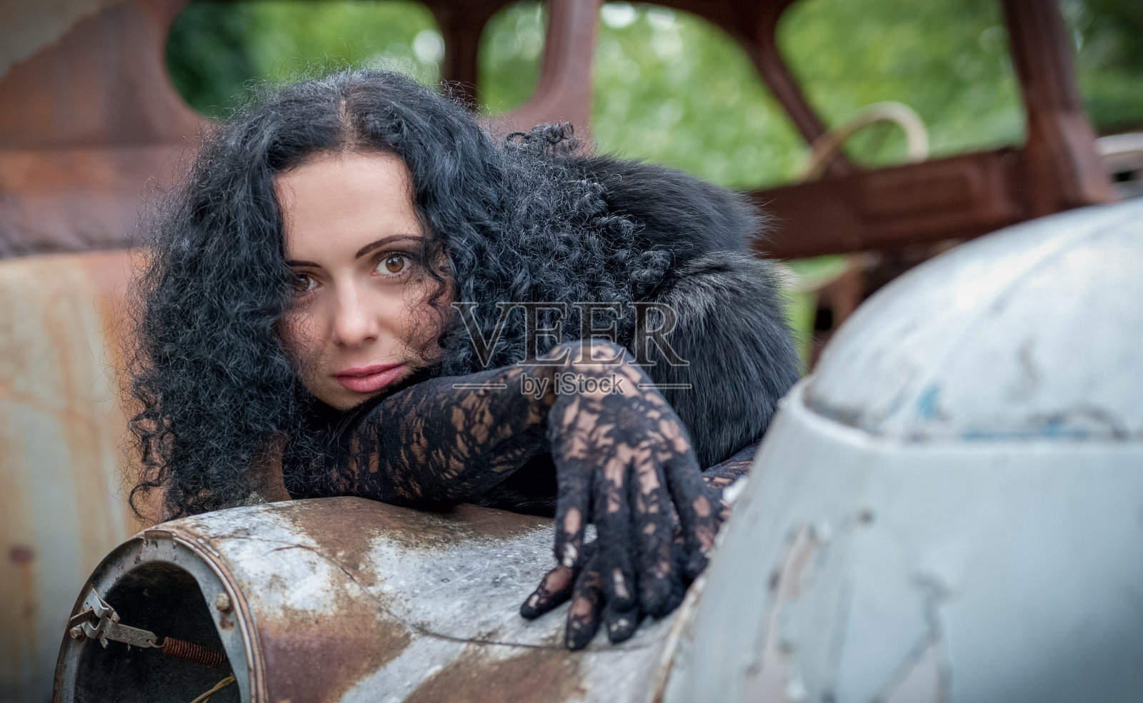 一个漂亮的年轻女孩坐在一辆破车的屋顶上。照片摄影图片