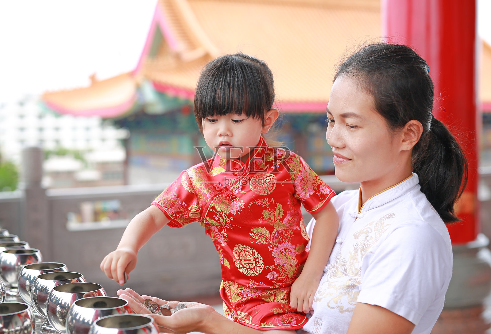 亚洲母亲和她穿着传统服装的女儿把硬币放在和尚的碗里。照片摄影图片