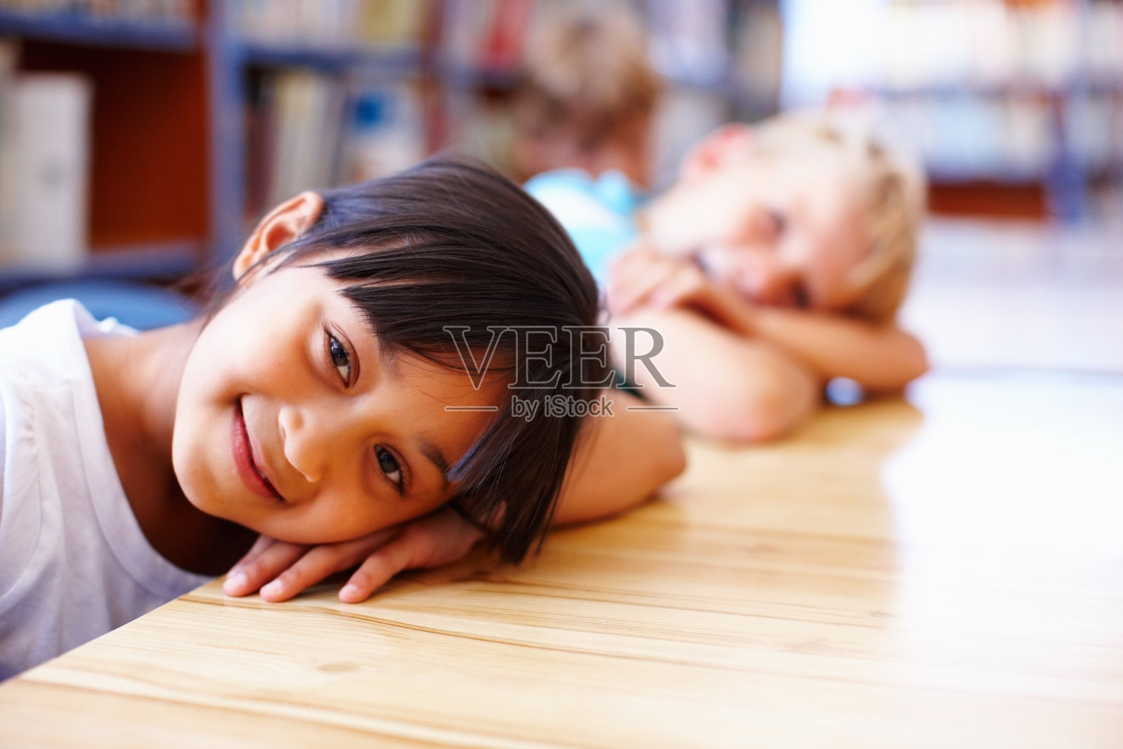 孩子们把头靠在图书馆的桌子上休息照片摄影图片