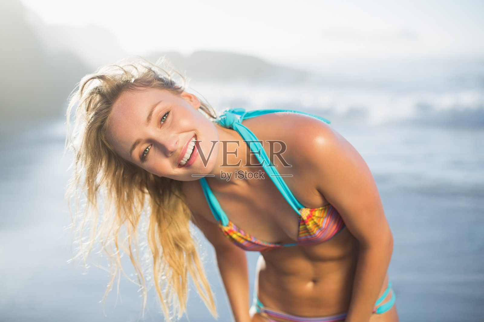 快乐的金发女郎穿着比基尼站在沙滩上照片摄影图片